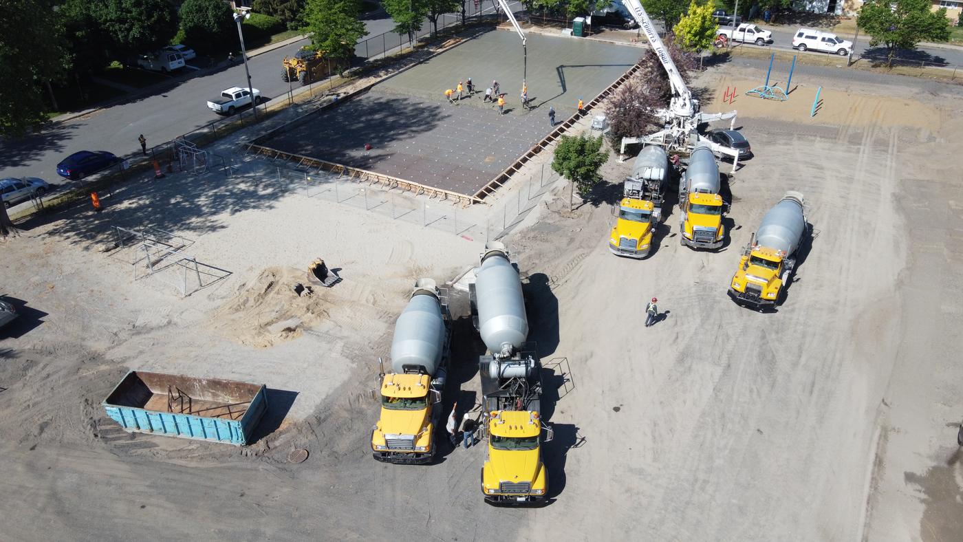 Vue aérienne de cinq bétonnières jaunes de Danis Construction et d'une pompe à béton pendant la coulée d'une dalle